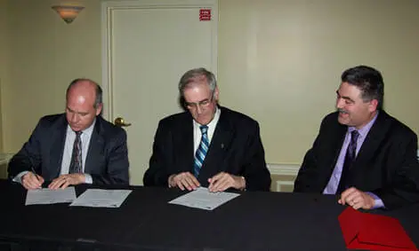 Three men signing documents at a table.
