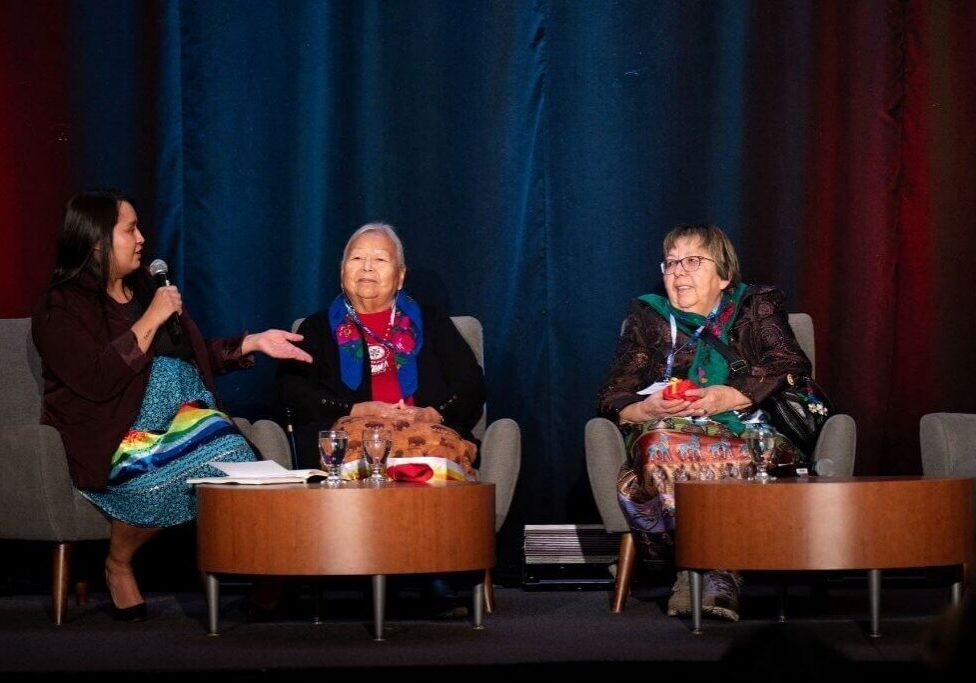 Three women conversing on stage with colorful backdrop