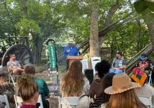 Audience seated outdoors under trees